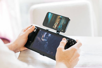 A person plays a game on the Steam Deck while watching a show on their phone mounted above the screen using the Mechanism Phone Mount.