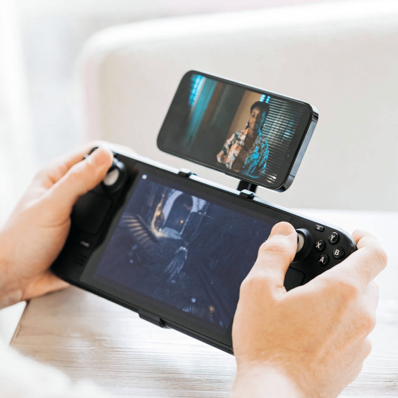 A person plays a game on the Steam Deck while watching a show on their phone mounted above the screen using the Mechanism Phone Mount.