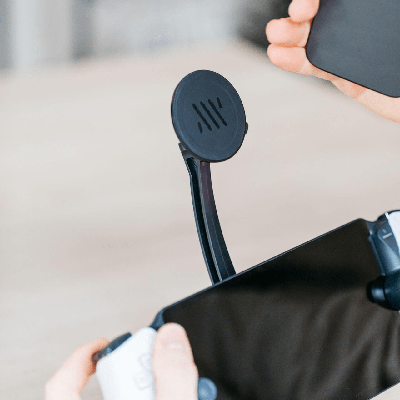 A person attaches their phone to the Magsafe arm of the Mechanism Phone Mount attatched to their gaming console