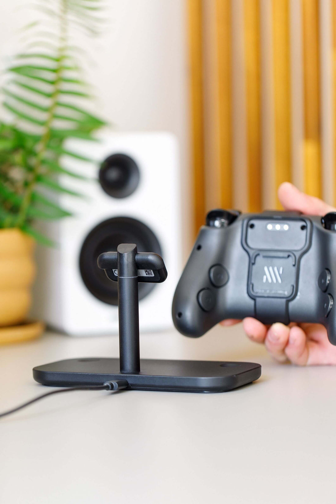 Hand holding a Steam controller next to a wireless charging stand on a desk.