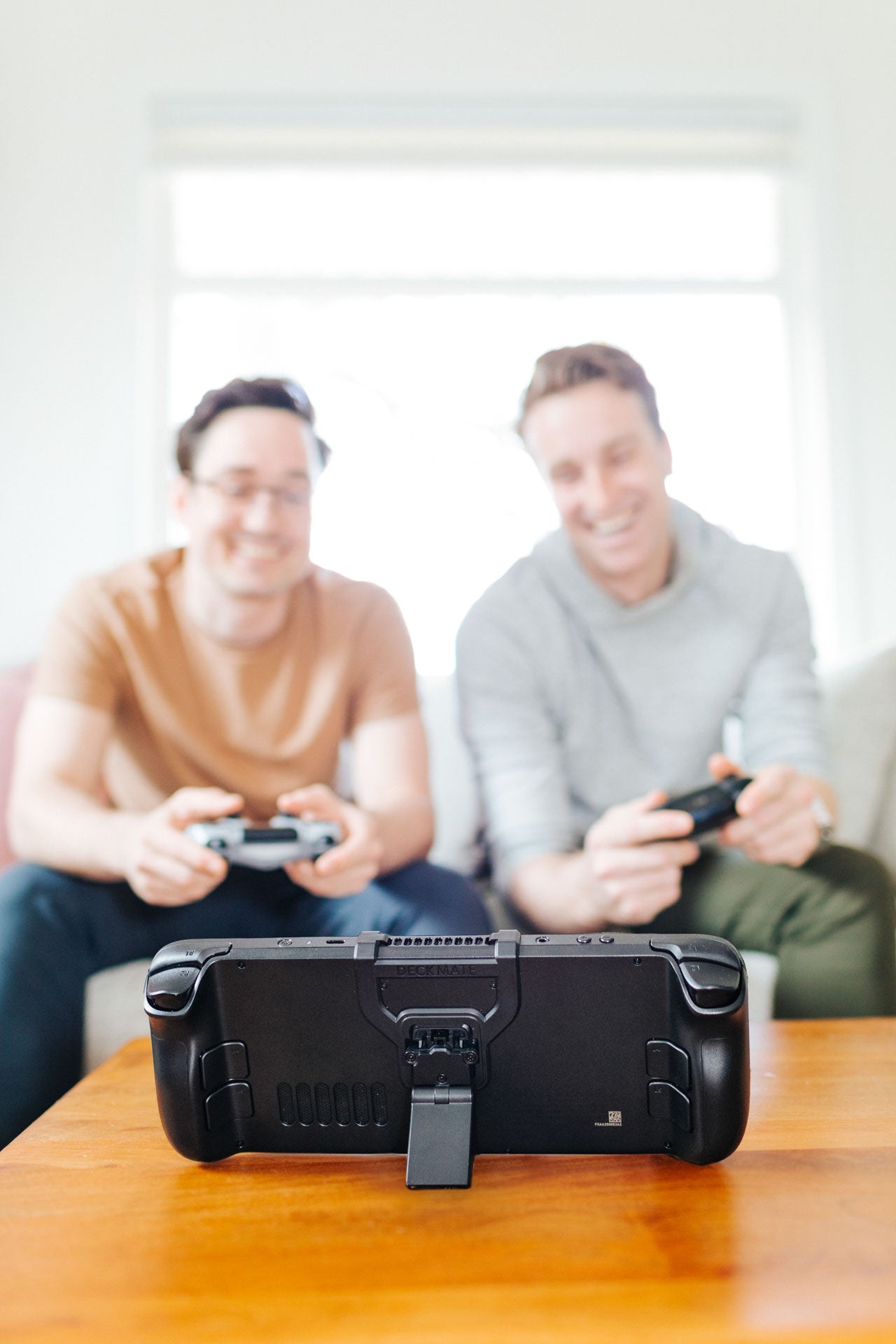 Friends play a game using controllers while their Steam Deck is propped on a table using the Steam Deck Accessory Deckmate Grip and Kickstand